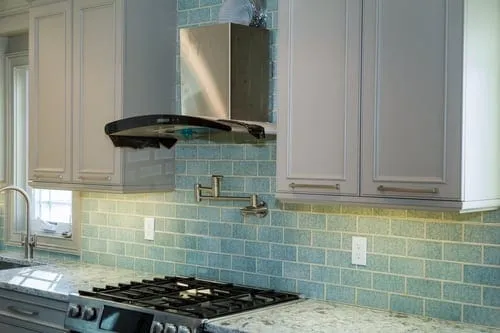 Kitchen backsplash with glass tile in blue-green tones behind the range and hood