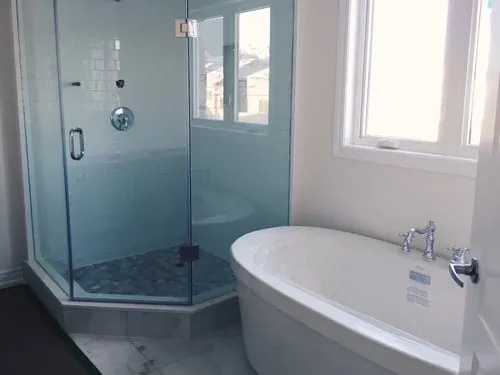 Glass shower door installed on a frameless tiled shower enclosure beside a freestanding tub
