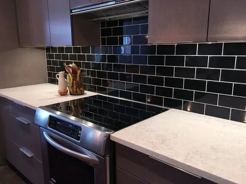 Kitchen backsplash tile installation in subway pattern behind a range with stone countertops